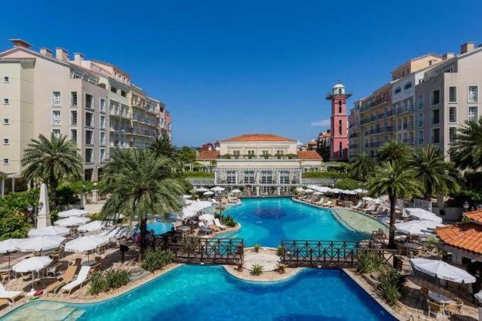 Luxury resort poolside view with palm trees, sun loungers, and Mediterranean-style hotel buildings.