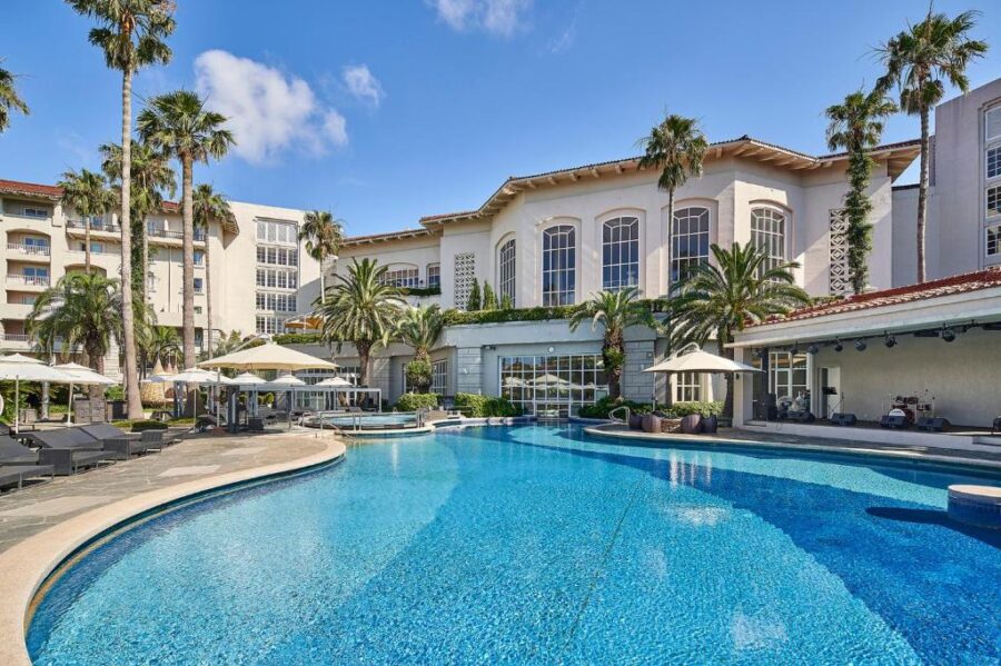 Luxury Jeju resort hotel with palm trees and infinity swimming pool under clear blue sky.