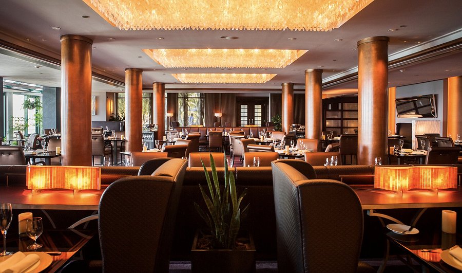 Upscale luxury restaurant interior with golden lighting, copper columns, elegant tables and leather seating.