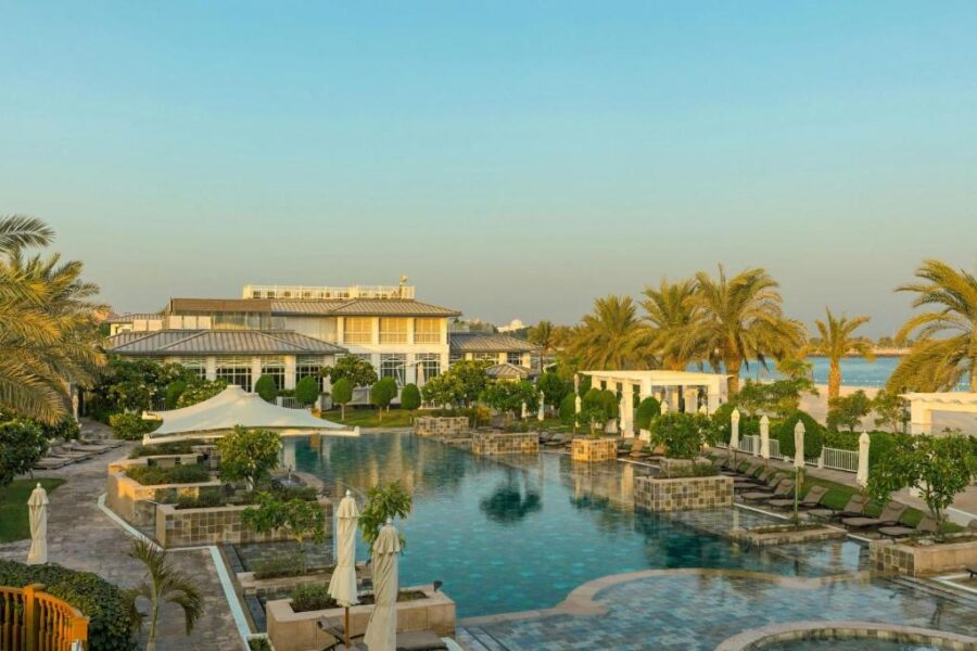Luxury Abu Dhabi beachfront resort pool at sunset with palm trees, cabanas, and ocean views.