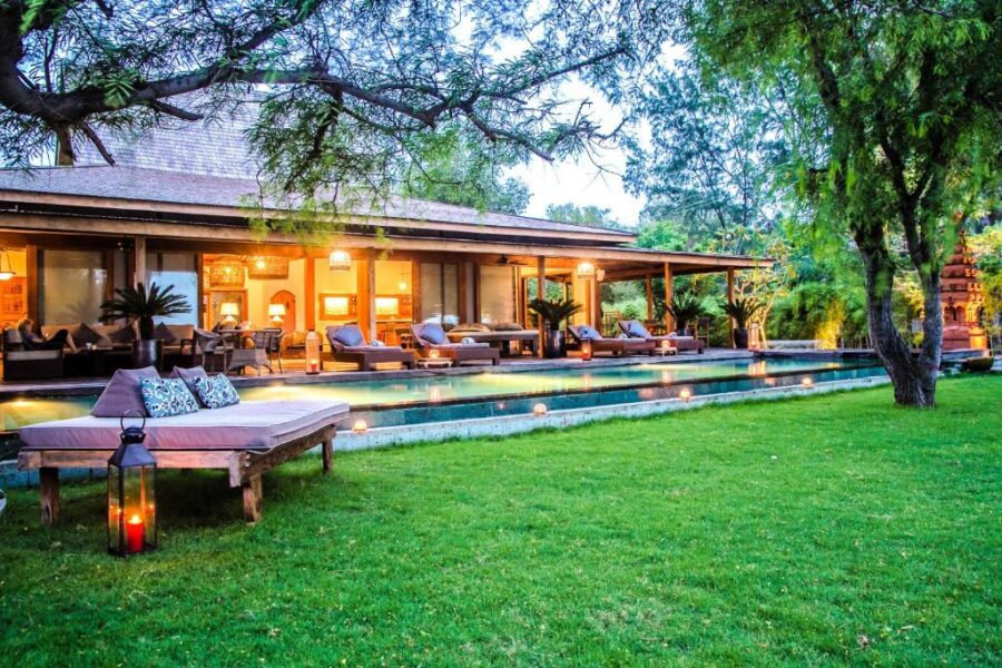 Luxury villa with illuminated pool, tropical garden, outdoor lounge chairs and daybed at dusk.
