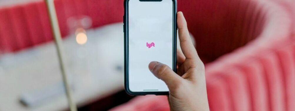 Hand holds smartphone with Lyft app in modern restaurant setting.