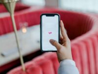 Hand holds smartphone with Lyft app in modern restaurant setting.