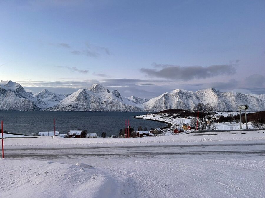Snowy Lyngen Alps in Norway with a serene lake visible in the background, showcasing a stunning mountain landscape.
