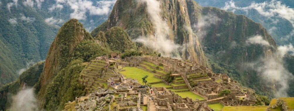 Machu Picchu ruins with lush mountains, terraces, and tourists amid clouds.