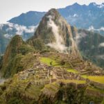 Machu Picchu ruins with lush mountains, terraces, and tourists amid clouds.