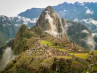 Machu Picchu ruins with lush mountains, terraces, and tourists amid clouds.