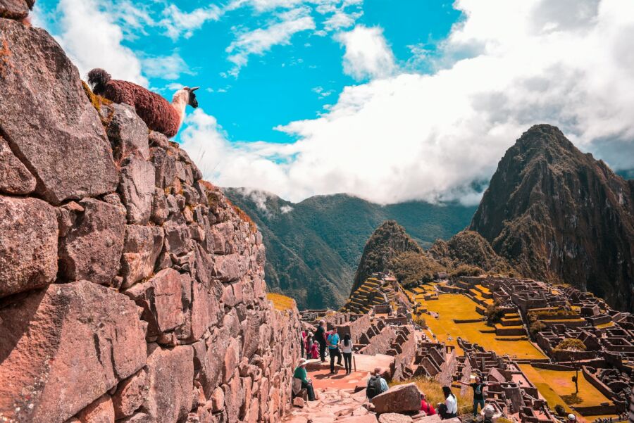 Breathtaking Machu Picchu ruins with mountains, lush greenery, stone walls, tourists, and a llama.