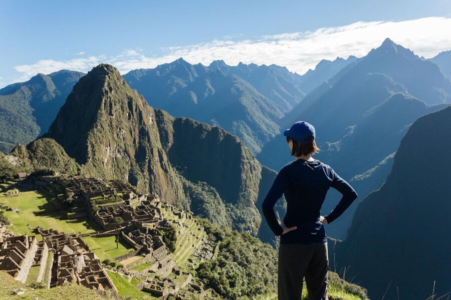 Machu Picchu ruins viewed by hiker; stunning Andes Mountains backdrop and lush terrain visible.