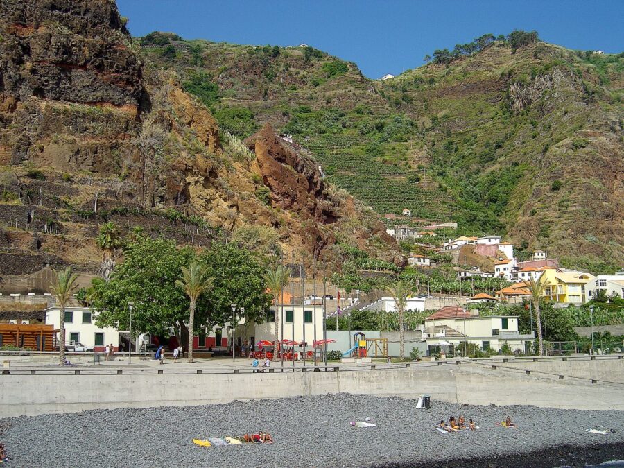 Picturesque beach scene in Madalena, Pico Island, with several people scattered along the shoreline.