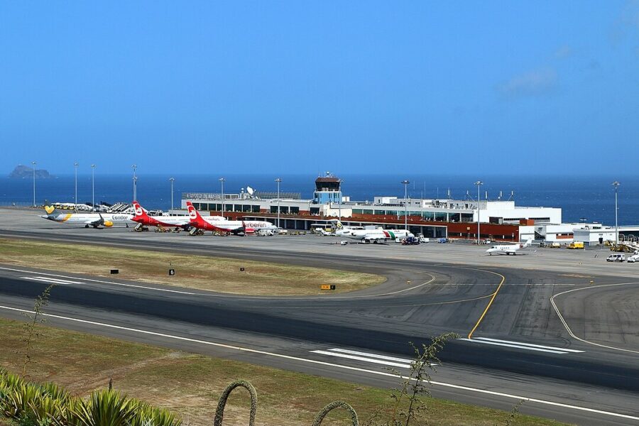 Aerial view of Madeira Airport featuring a runway beside a large body of water, showcasing the scenic landscape.
