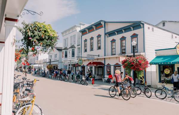 Historic Mackinac Island main street with Victorian shops, tourists, and parked bicycles on a sunny day.