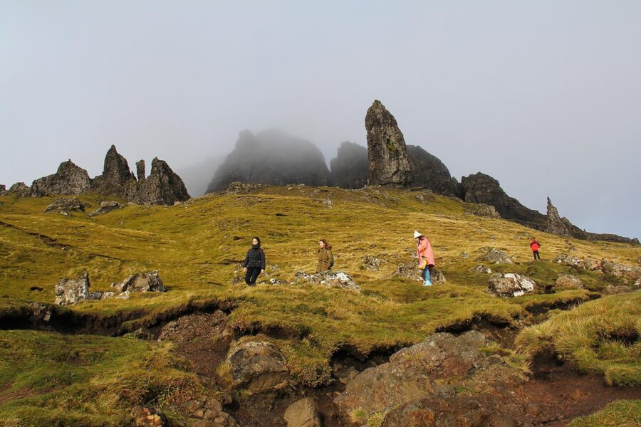 Adventurers exploring misty rugged mountain landscape with towering rock formations and lush green slopes.