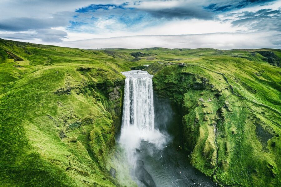 Majestic waterfall in lush Icelandic landscape with cliffs and greenery.