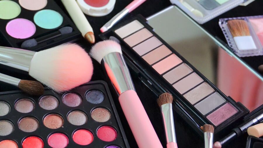 Variety of cosmetics displayed, including colorful eyeshadow palettes, pink makeup brushes, and lip glosses, evoke a vibrant and creative beauty setup.