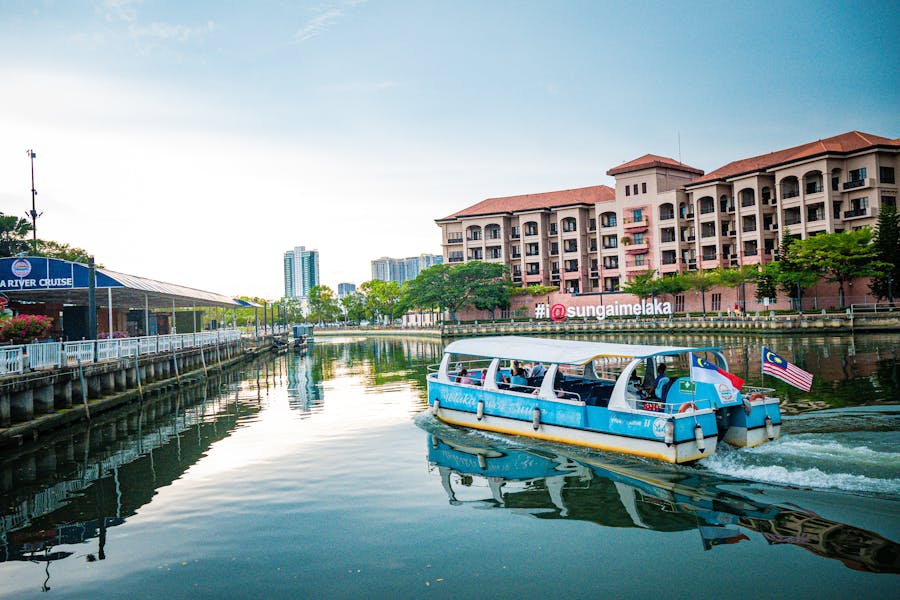 Melaka river cruise with Malaysian flag boat, urban buildings, and tranquil nature.