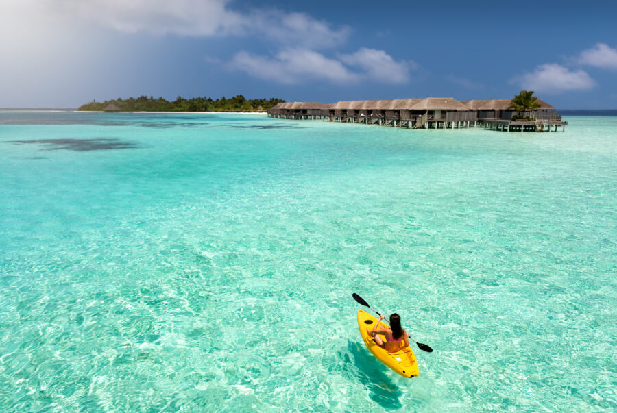 Woman paddling a kayak through the clear turquoise waters of the Maldives, surrounded by a tropical paradise