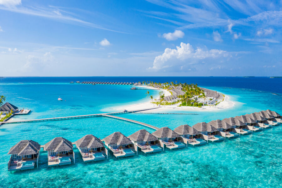 Aerial view of a luxury tropical resort in the Maldives, featuring water villas and stunning beach scenery