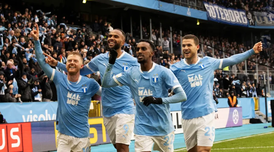 Malmo FF players celebrating a goal in blue kits with cheering fans in stadium.