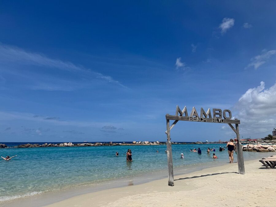 The sign for "Mambo Beach" is displayed on the beach at Mambo Beach, Curacao, highlighting the Caribbean landscape.

