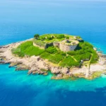 Aerial view of Mamula Island in Montenegro, showcasing a historic fortress bathed in sunlight against a clear blue sky