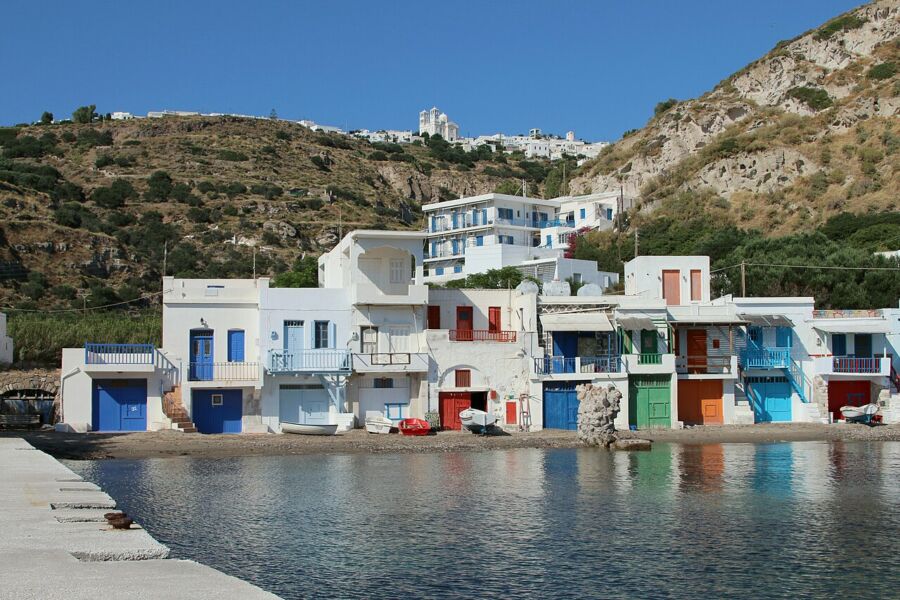 Colorful houses line the shore of a tranquil body of water in Mandrakia, Greece, creating a picturesque coastal scene.