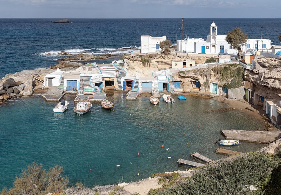 Several boats are moored in the picturesque harbor of Mandrakia, Milos, Greece, with vibrant colors reflecting on the water.