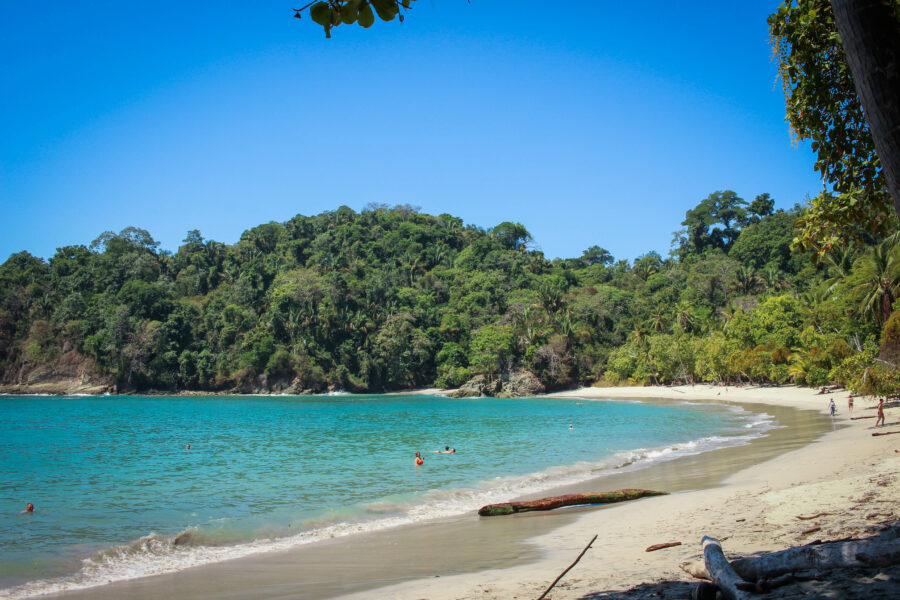 Scenic panorama of Manuel Antonio Beach, featuring vibrant blue ocean waves, sandy shores, and surrounding tropical vegetation