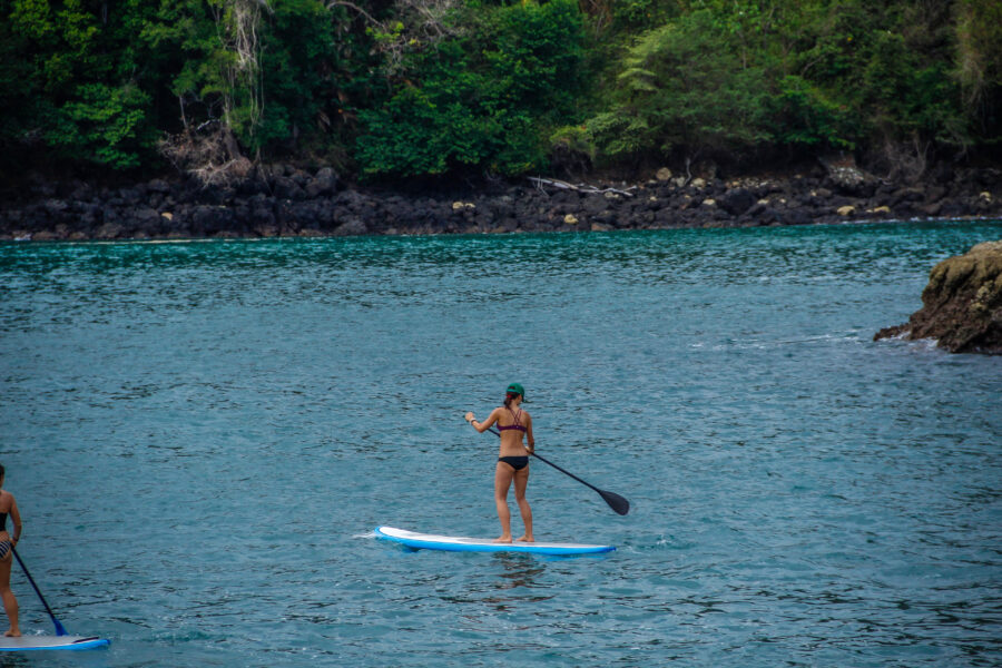 Young woman paddle surfing in the calm waters of Manuel Antonio National Park, surrounded by lush greenery