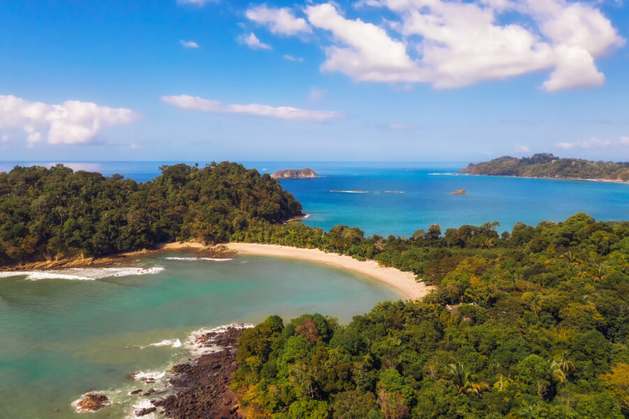 Scenic aerial shot of a beach framed by dense foliage in Manuel Antonio National Park, showcasing Costa Rica's natural beauty