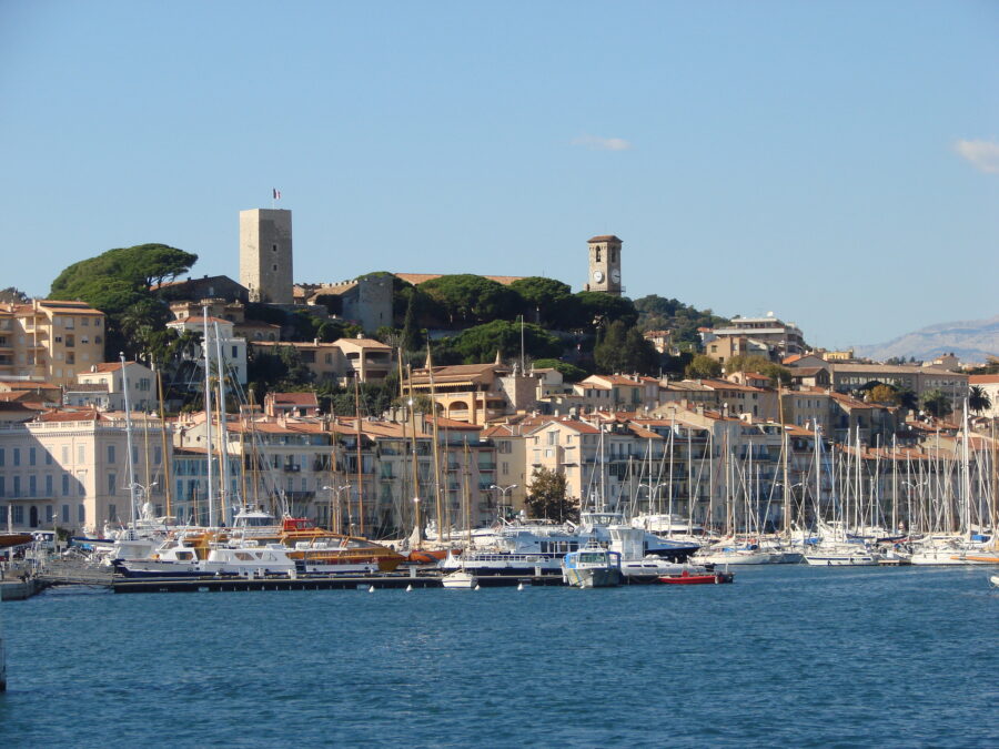 Picturesque Mediterranean harbor with boats, pastel buildings, clock tower, and lush hills.