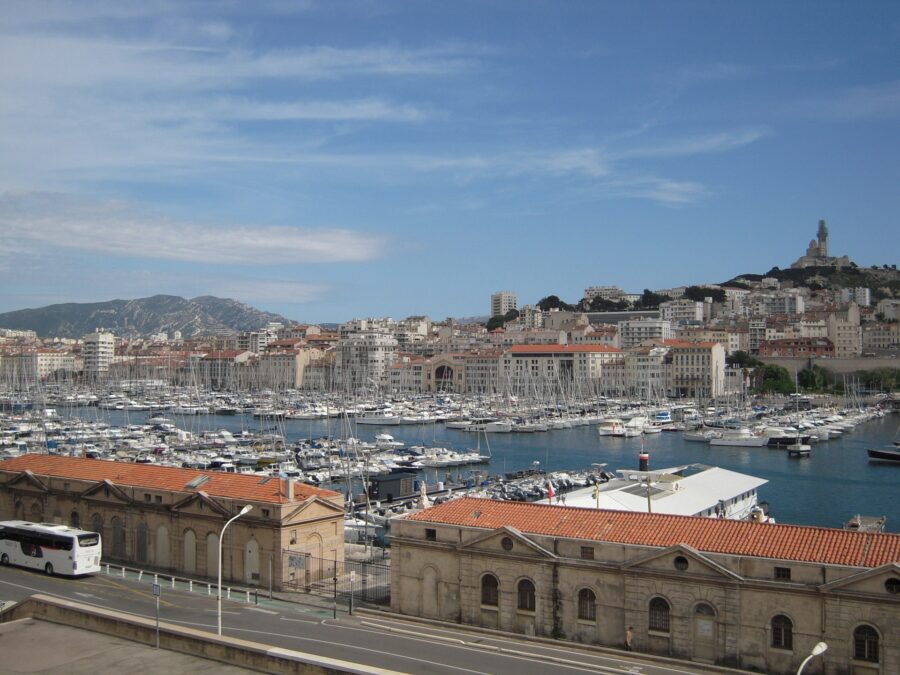 Marseille marina and harbor with moored boats and historic hilltop basilica skyline.