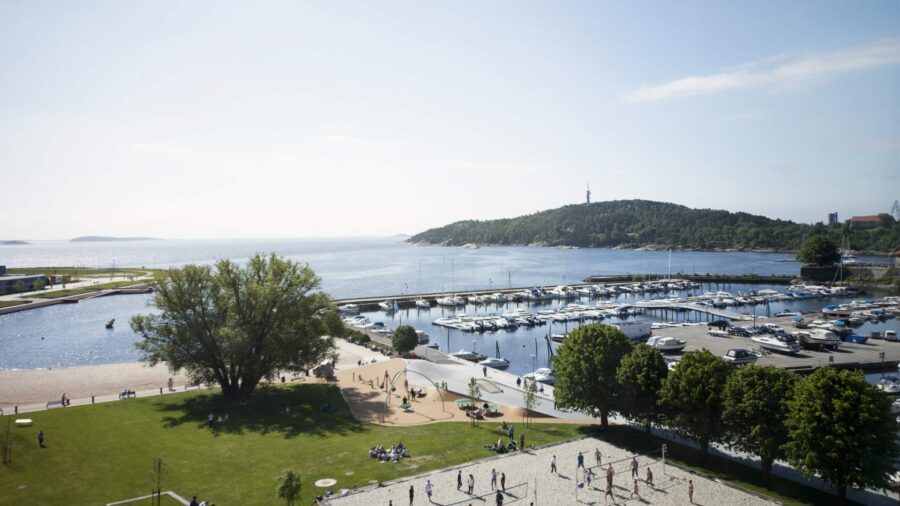 Marina park seaside with sailboats, harbor, beach, playground and people enjoying coastal views.