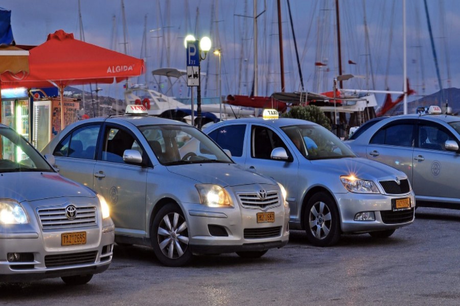 Silver taxis lined at Milos marina at twilight with yacht masts and wet harbor pavement.