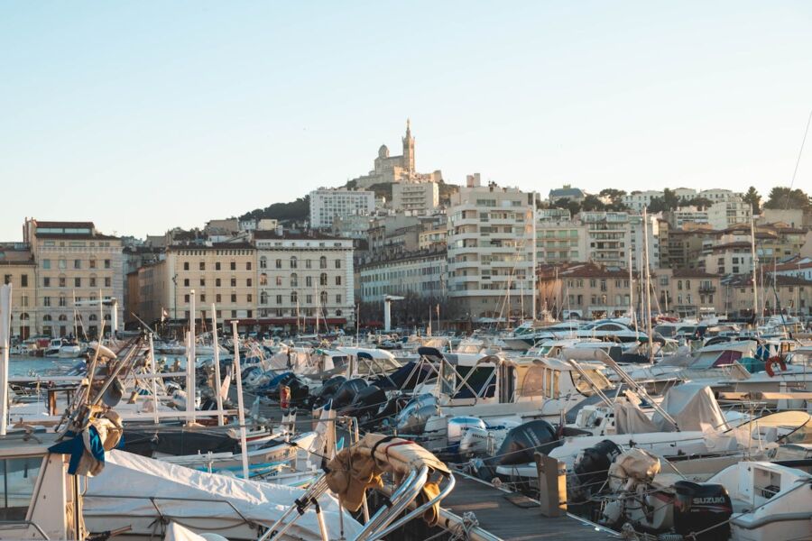 Picturesque marina with boats, yachts, hillside buildings, and historic structure during golden hour.