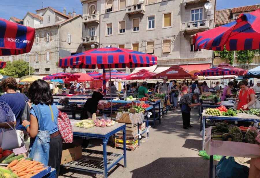 Bustling open-air market scene with fresh produce, vibrant colors, and diverse crowd activity.