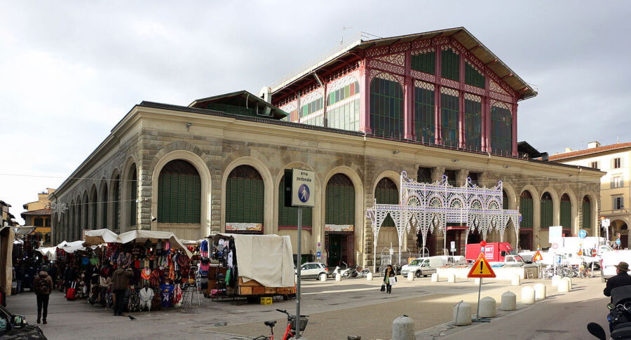 Bustling urban market with mixed architecture, vibrant stalls, pedestrians, and overcast sky.