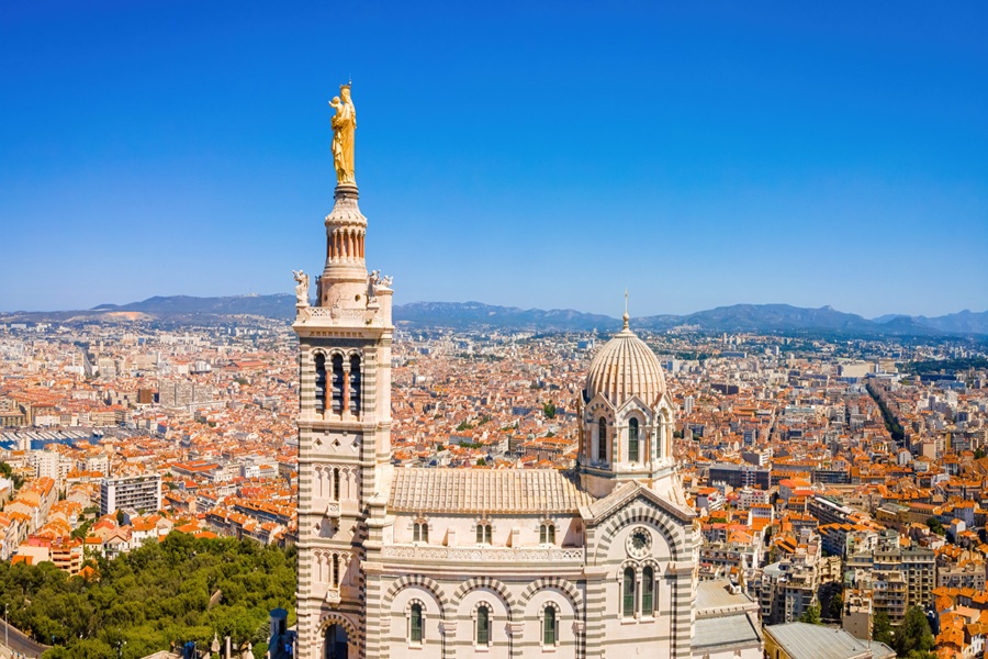 Aerial view of Notre-Dame de la Garde Basilica, Marseille, with cityscape and Mediterranean backdrop.