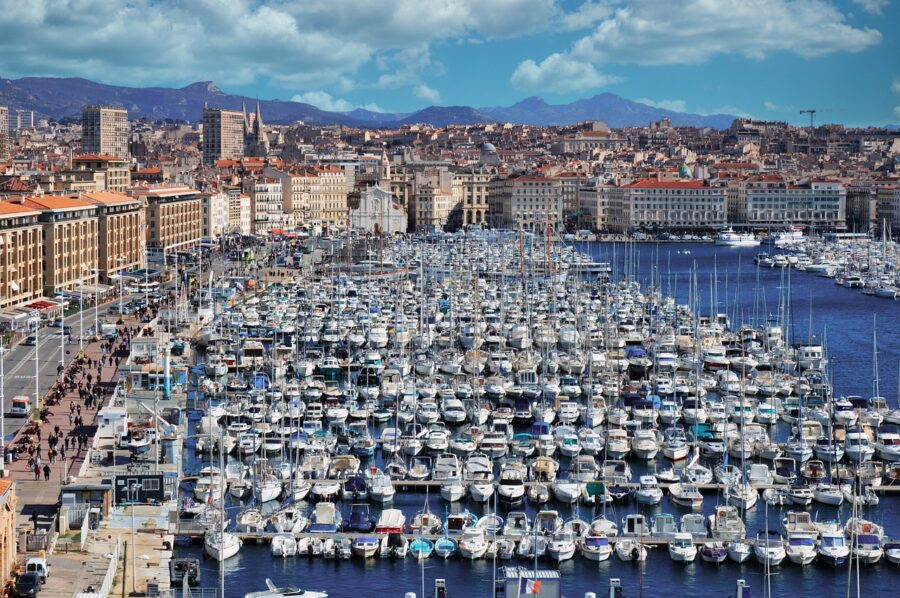 Bustling Marseille marina with yachts, Mediterranean architecture, and mountain backdrop.