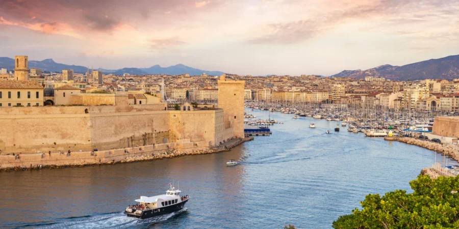 Marseille harbor sunset: boats, stone fortifications, cityscape, picturesque Mediterranean coast.