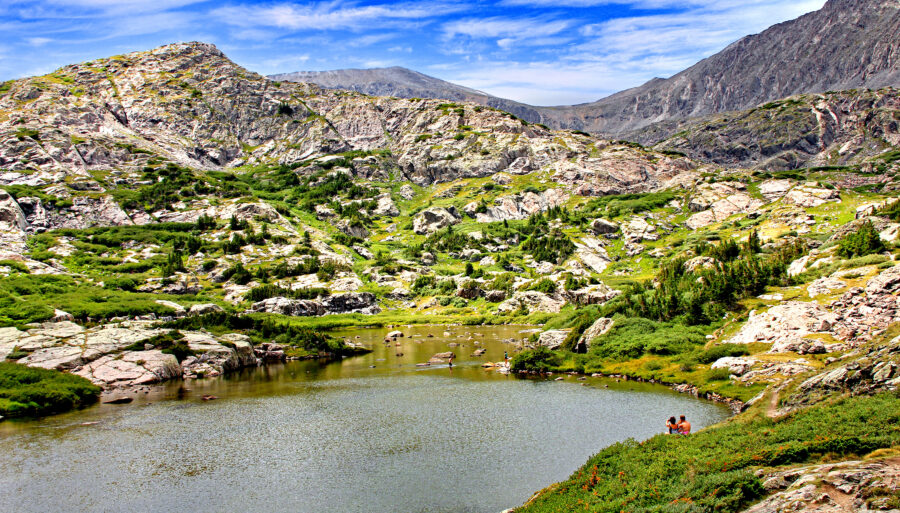 Hikers relax by a serene alpine lake at the summit of McCullough Gulch Trail in Colorado near Breckenridge