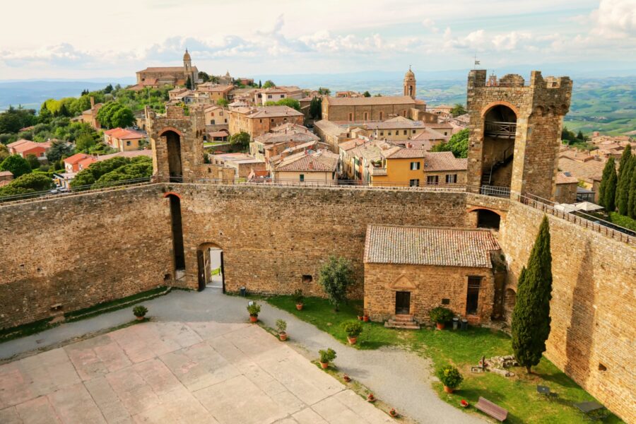 Medieval Tuscan hilltop village with stone fortifications, church spire, and lush landscape.