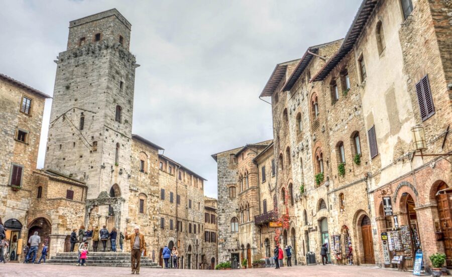 Medieval San Gimignano square with tourists, stone tower, architecture, cobbles, and local culture.