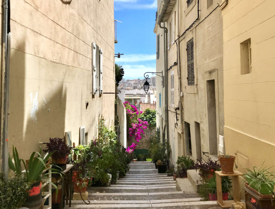 Sunlit Mediterranean alley with vibrant potted plants and historic architecture.