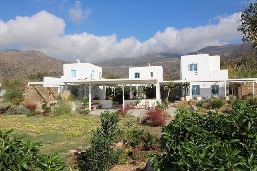 Charming Mediterranean white house complex with blue accents amidst lush gardens and scenic hills.