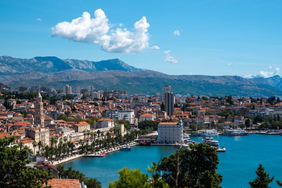 Picturesque Croatian coastal town with terracotta roofs, palm-lined promenade, and stunning mountainous backdrop.