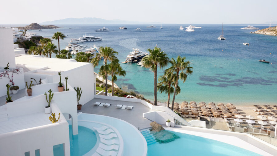 Luxurious Mykonos resort with infinity pool, palm trees, yachts, and stunning coastal views.