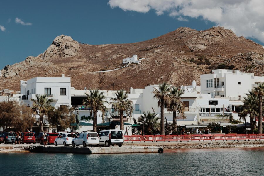 Mediterranean coastal town with palm-lined harbor, white buildings, and mountain backdrop.