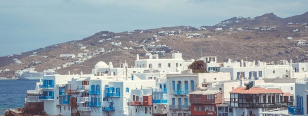 Picturesque Greek seaside town with white architecture, blue shutters, and calm waters.