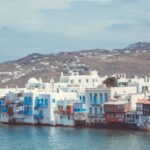 Picturesque Greek seaside town with white architecture, blue shutters, and calm waters.